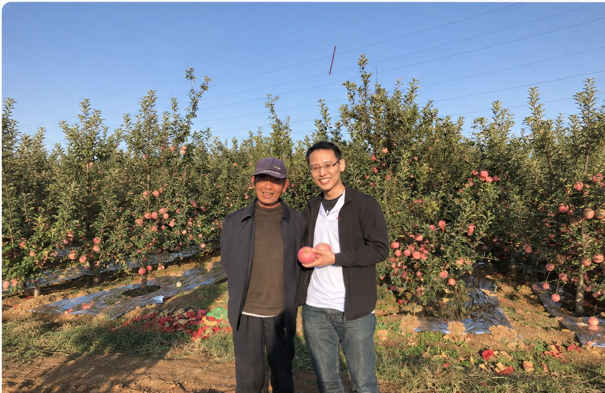 Two people during a 3YY Fresh orchard sourcing visit in China, with an expansive view of the orchard